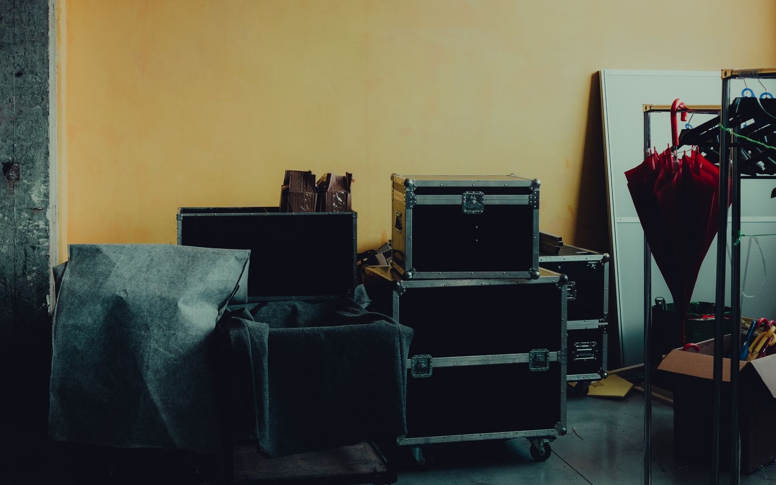 Stacked black flight cases and covered equipment against a yellow wall backstage